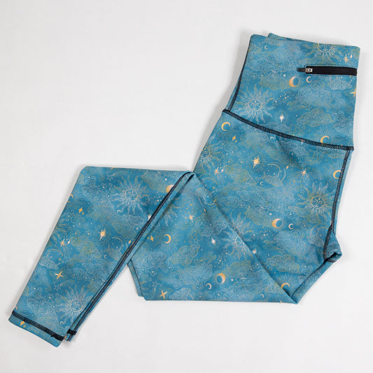 Blue patterned leggings with a celestial print of stars, moons, and suns, laid flat on a white background.